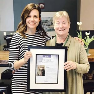 Carol Chase and April Hulst hold up a framed version of the GRBJ article that marks them as a top woman led business.